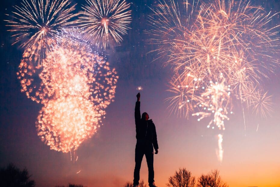 man holding sparkler in front of fireworks
