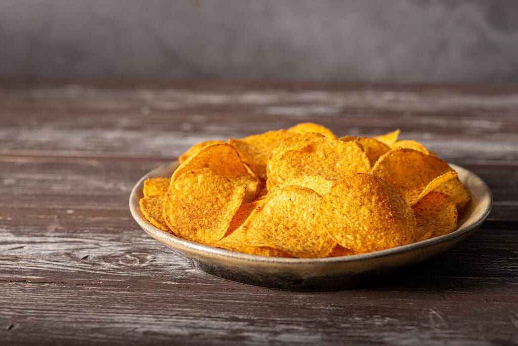 A bowl of high calorie potato chips sitting on a wooden table.