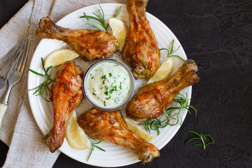 Oven roasted chicken drumsticks rest on a plate with lemon and garnish next to a bowl of homemade ranch.